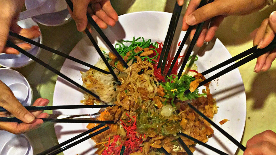 Group of people reaching into a plate of food with chopsticks