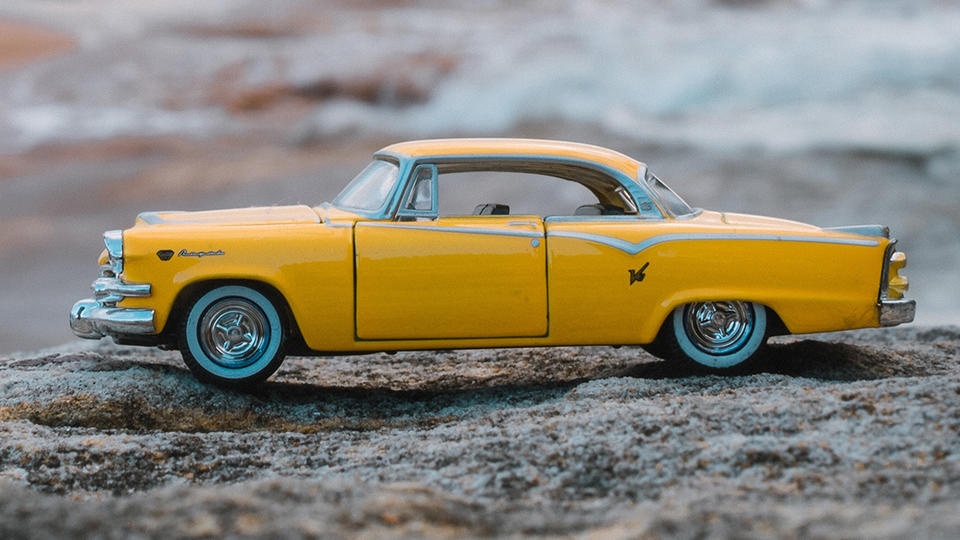 A toy car on a rock at the beach.