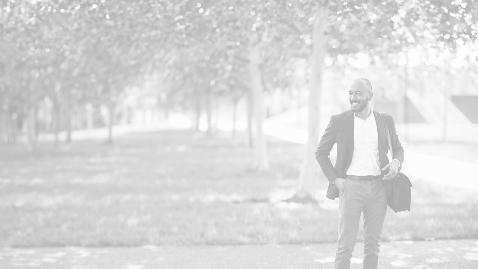 Man smiling with a shoulder bag standing outside. 