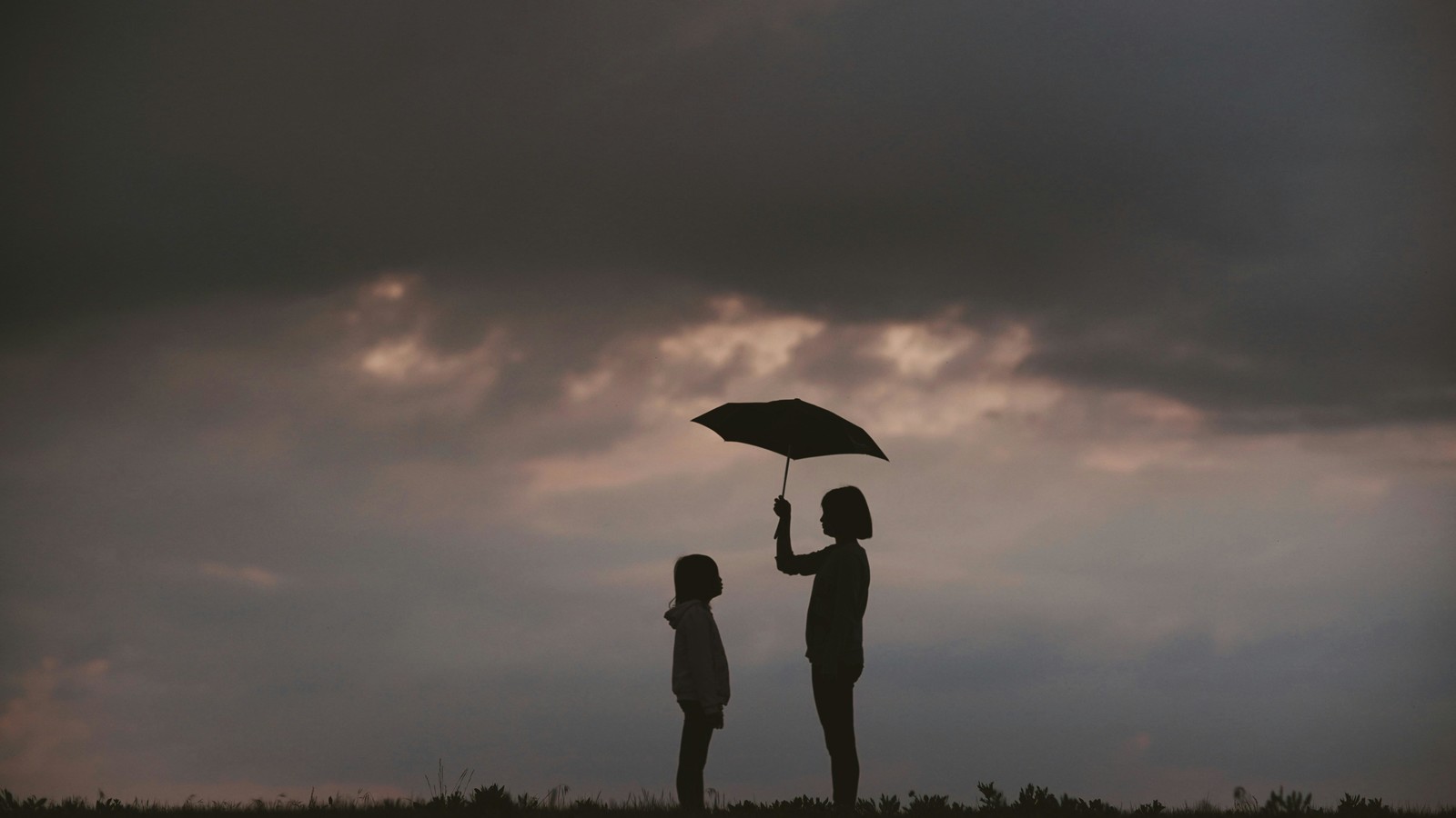 One person holding an umbrella over the other