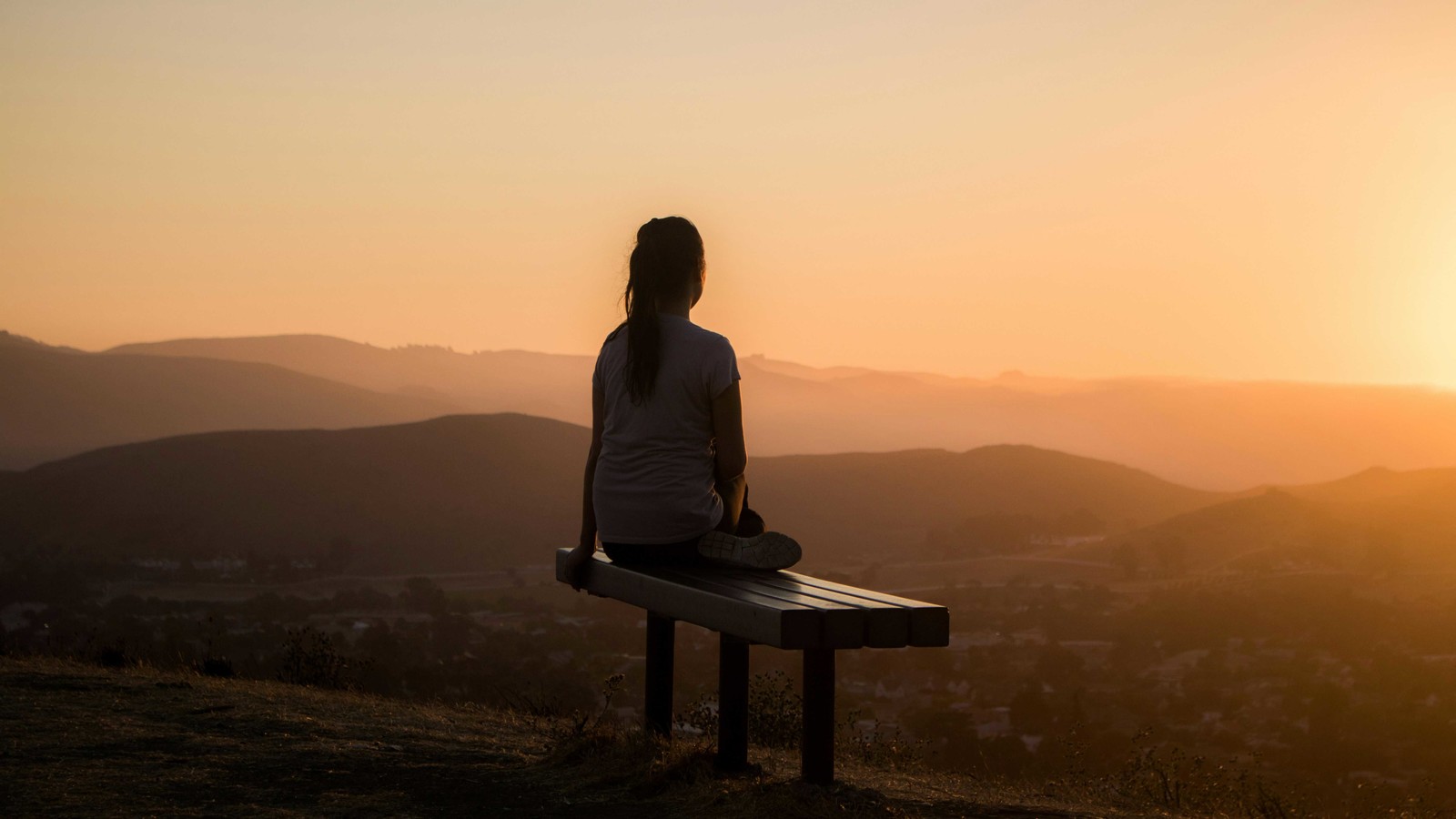 Woman sitting on bench looking at sunset