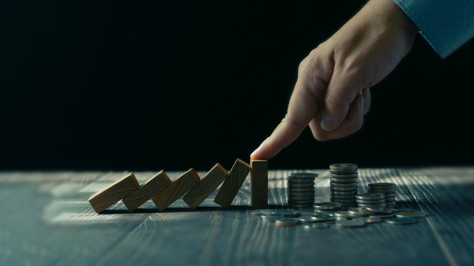 Hand stops a row of dominoes from tipping over onto a pile of coins