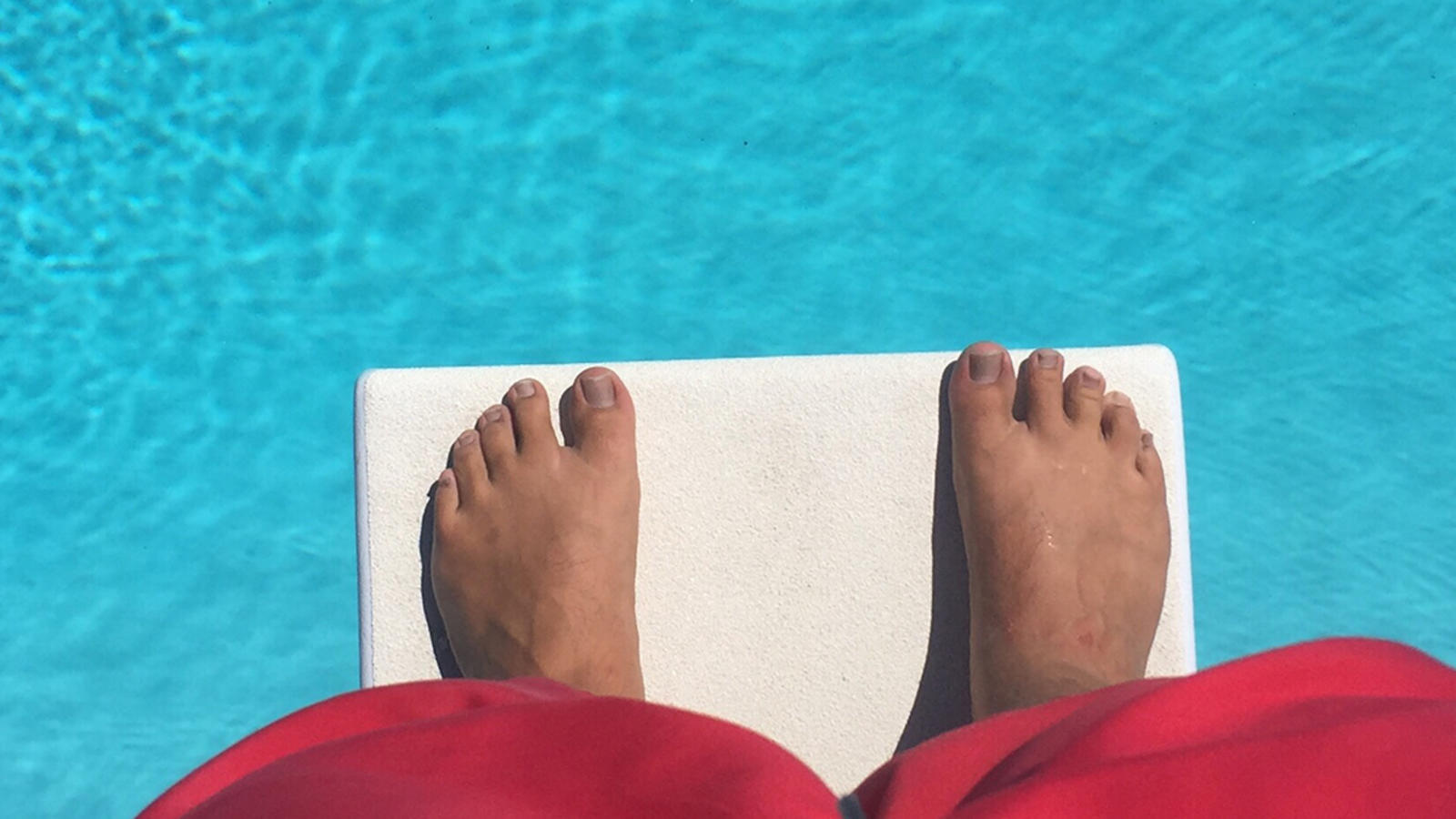 Person standing at the edge of a pool diving board