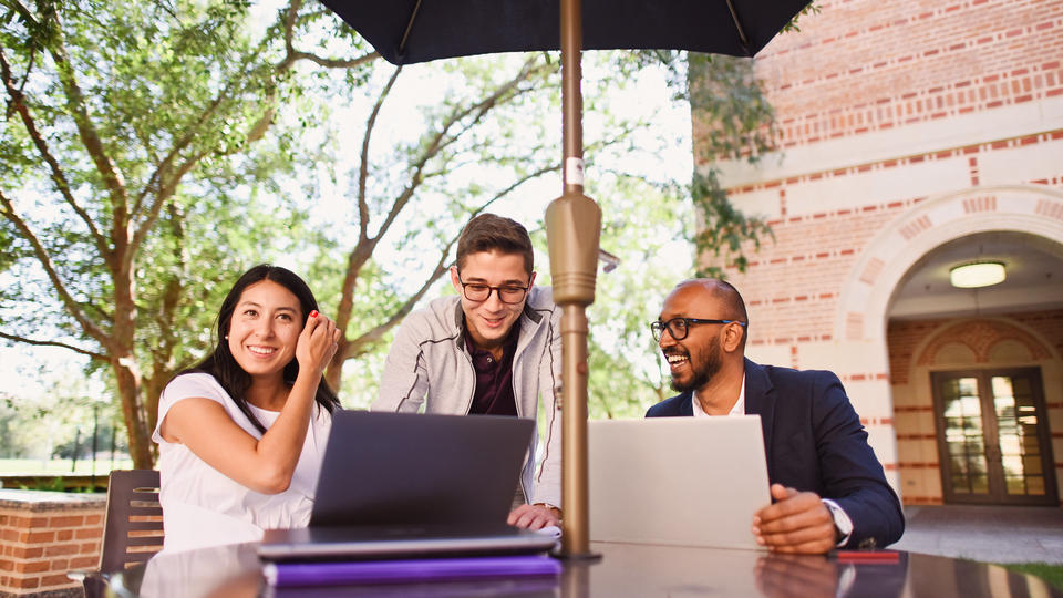 Three students sitting outside looking at laptop