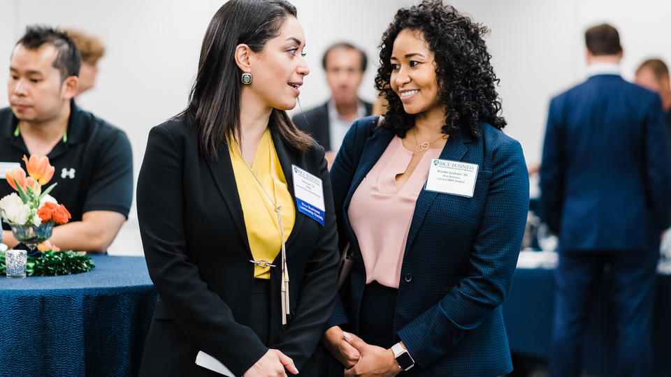 Female MBA student in yellow blouse speaking with female MBA student in pink blouse