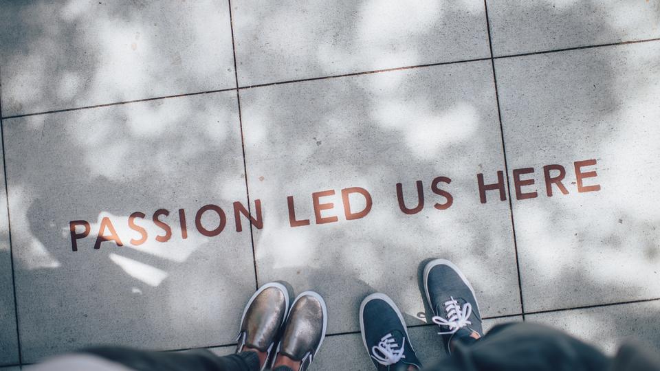 Two people standing next to "Passion Led Us Here" graffiti 