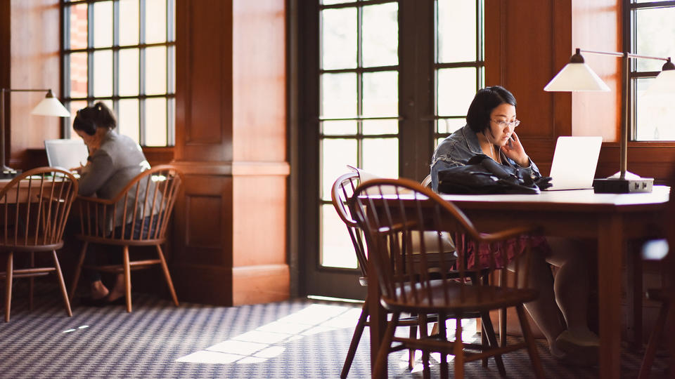 female student with glasses working at table in library on laptop