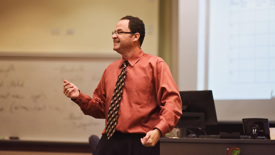 Professor K. Ramesh in orange button down and tie teaching to class