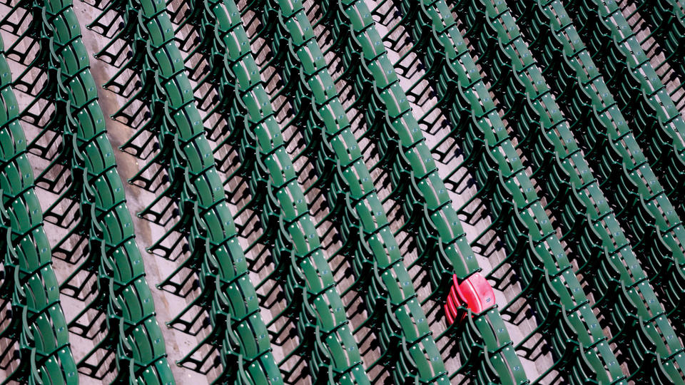One red stadium seat among many green stadium seats