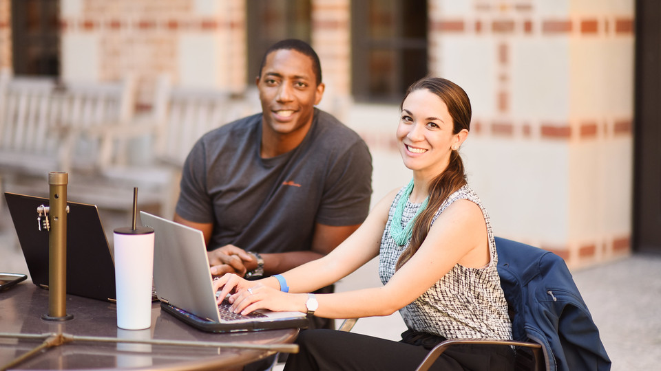 Two students sitting at a table looking at a laptop