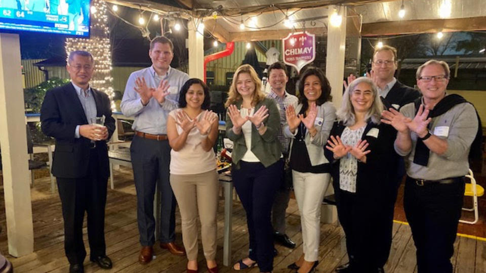 Group of alumni standing in a line doing "owl hands" outdoors at a bar