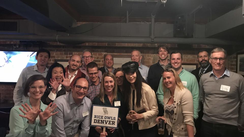 Group of alumni in a dark bar with a sign saying "Rice Owls Denver"
