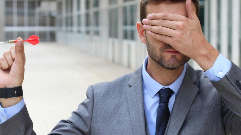 Man wearing business suit holding a dart with his eyes covered