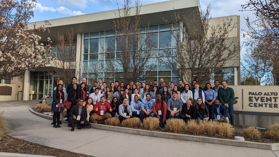 Group of 100 students posing in front of a glass building