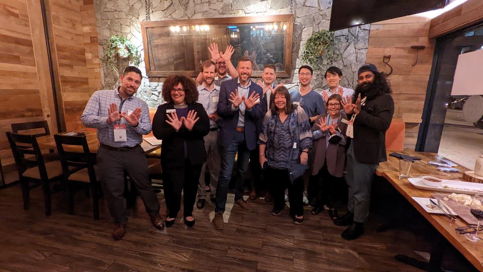 Group of staff and alumni standing in front of tables holding up 'owl hands'