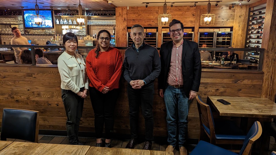 Three alumni and Dean Peter Rodriguez standing in a row smiling with hands clasped