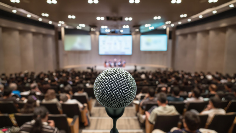 A microphone at the center with conference room audience on either side.