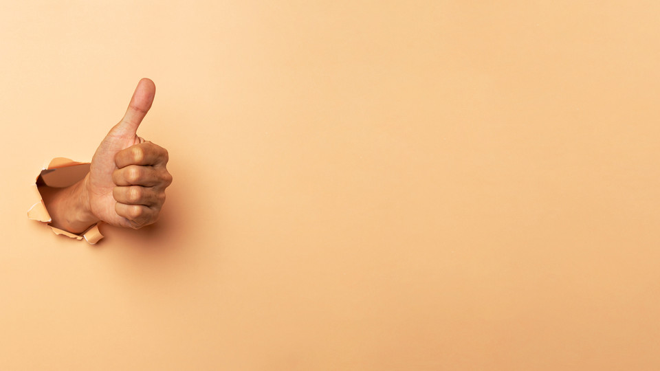 Thumb up punching through yellow wall