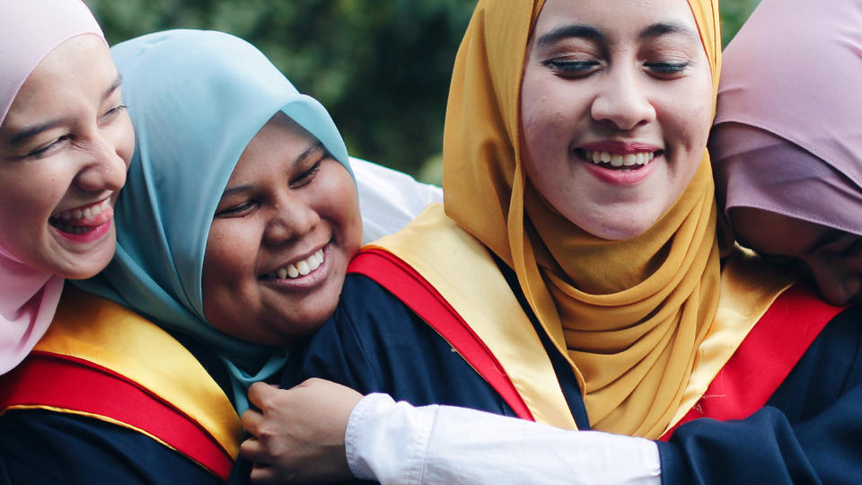 Group of women in graduation gowns hugging. 