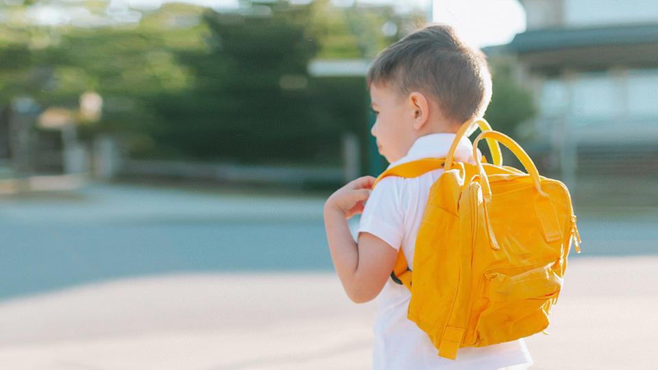 Young boy with a yellow backpack waiting for a bus. 