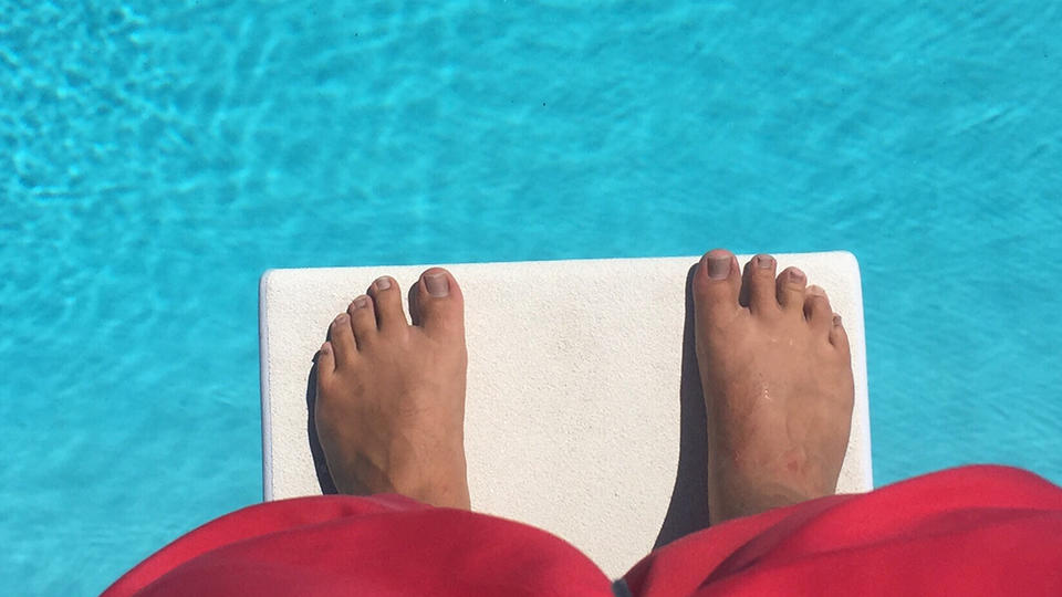 Person standing at the edge of a pool diving board 