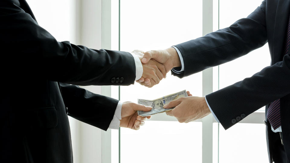 Two people in suits shaking hands while one is handing money to the other. 