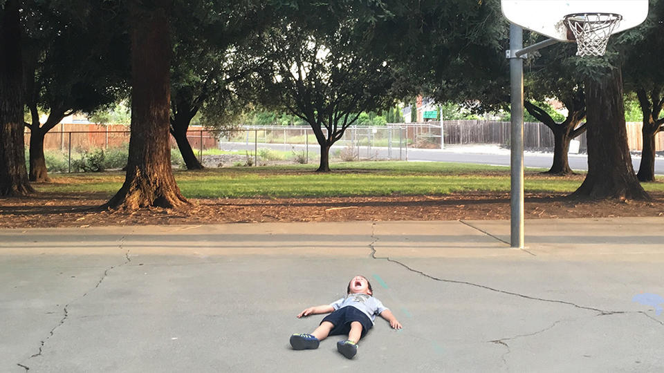 Boy laying on basketball court, crying. 