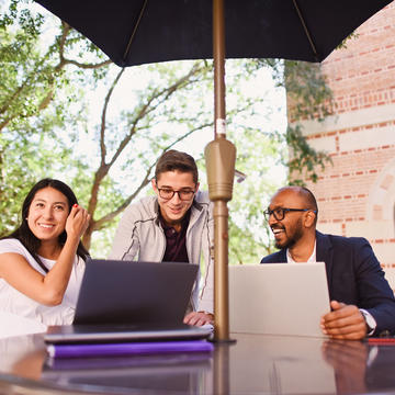 Three students sitting outside looking at laptop