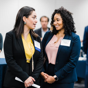 Female MBA student in yellow blouse speaking with female MBA student in pink blouse