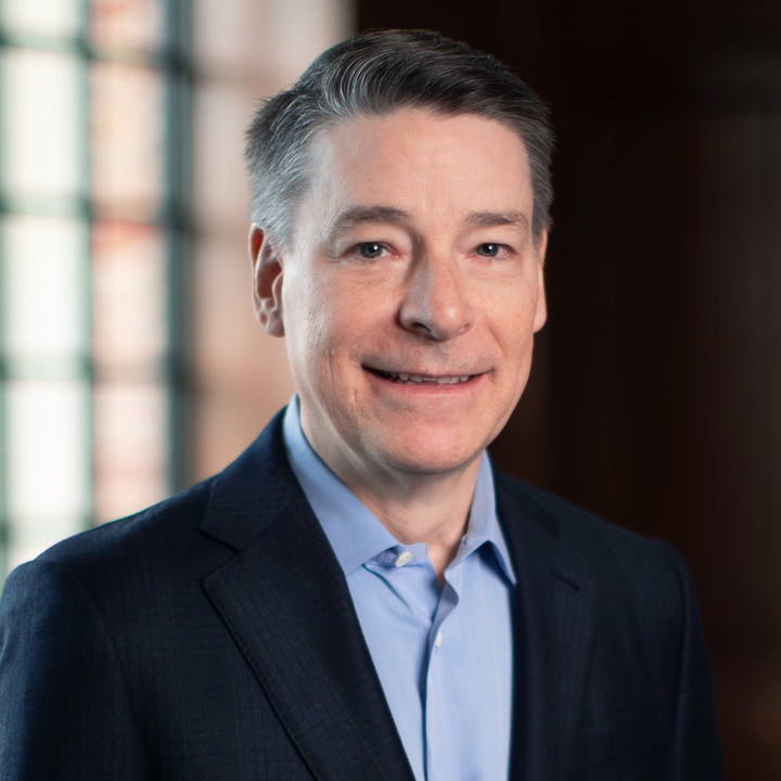 A man, Jeff Fleming, in a dark suit and smiling with a window behind him. 