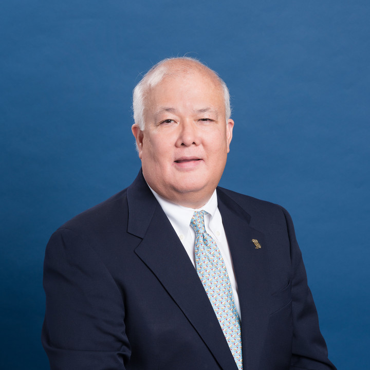 Photo of a man in a dark suit and light blue tie. 